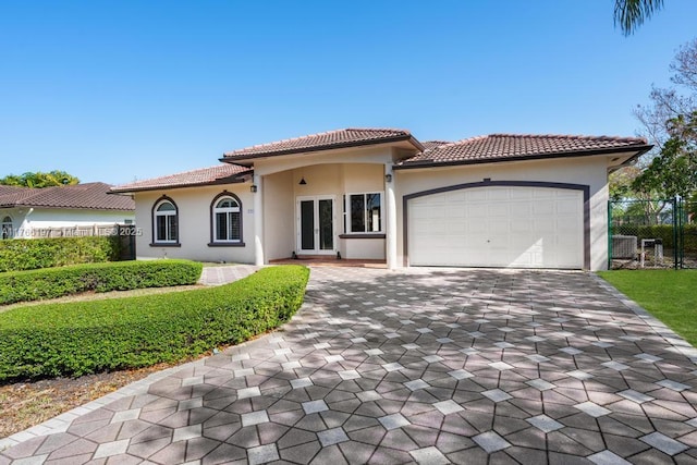 mediterranean / spanish-style home with a tile roof, fence, stucco siding, and decorative driveway