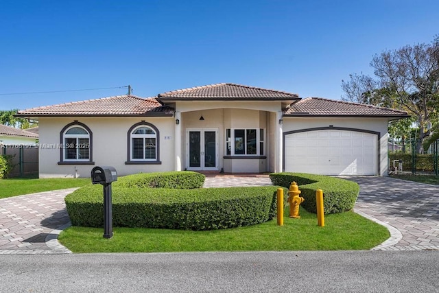 mediterranean / spanish-style house featuring fence, a tiled roof, stucco siding, an attached garage, and french doors