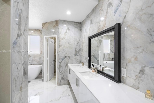 bathroom featuring a freestanding bath, tile walls, marble finish floor, and a sink