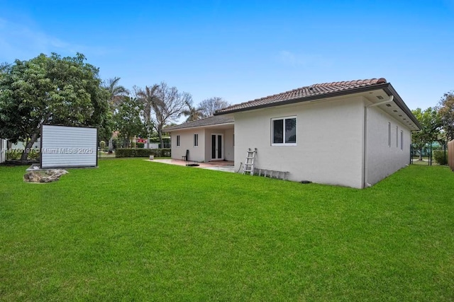 rear view of property featuring a lawn, a patio, a tile roof, and stucco siding