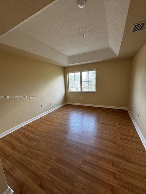 1017 Shoma Dr Unit 462, Royal Palm Beach, FL 33414 - empty room featuring a textured ceiling, wood finished floors, a raised ceiling, baseboards, and visible vents