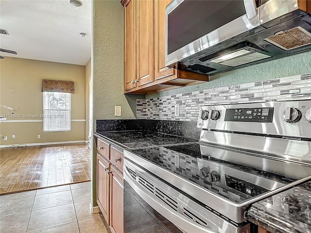 375 SW Dustin Ave, Port St Lucie, FL 34953 - kitchen with a textured wall, appliances with stainless steel finishes, brown cabinetry, light tile patterned floors, and tasteful backsplash