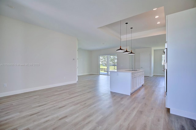 kitchen featuring baseboards, open floor plan, light wood-type flooring, and a raised ceiling