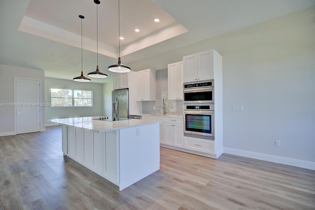 kitchen with baseboards, a sink, a raised ceiling, and appliances with stainless steel finishes