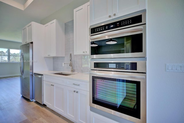 kitchen with tasteful backsplash, a sink, light wood-style floors, white cabinets, and appliances with stainless steel finishes
