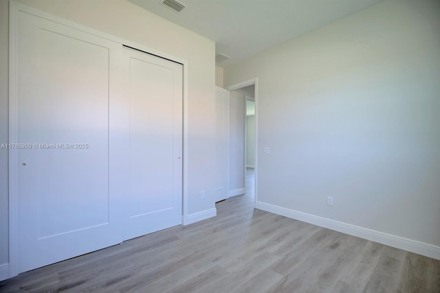 unfurnished bedroom with baseboards, visible vents, light wood finished floors, and a closet