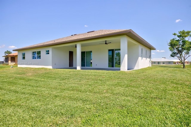 rear view of property featuring stucco siding, ceiling fan, and a lawn