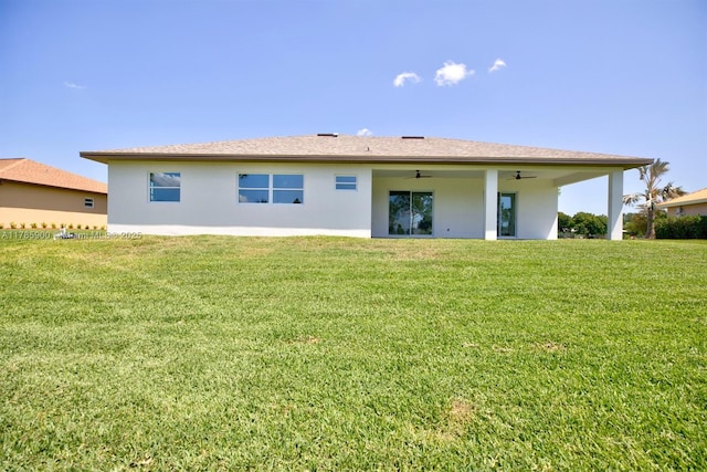 rear view of property with a ceiling fan, a yard, and stucco siding