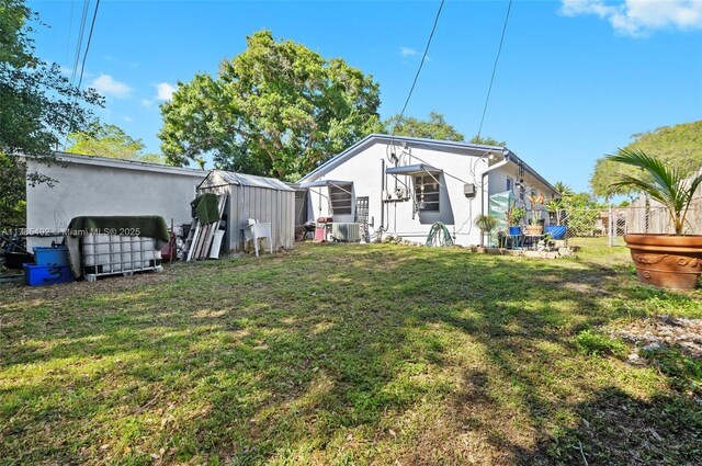 rear view of property featuring stucco siding, fence, a yard, and a storage shed
