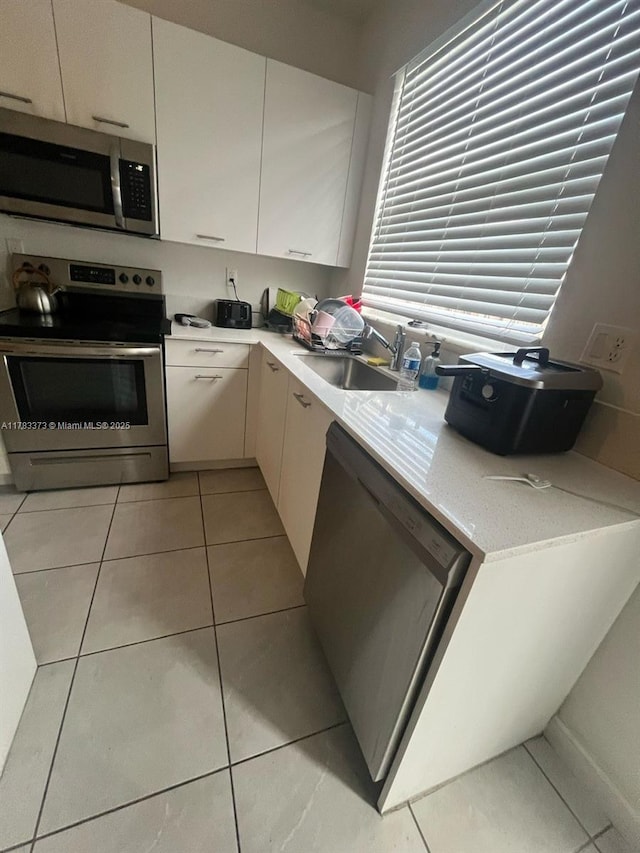 kitchen with a sink, light tile patterned floors, white cabinetry, light countertops, and appliances with stainless steel finishes