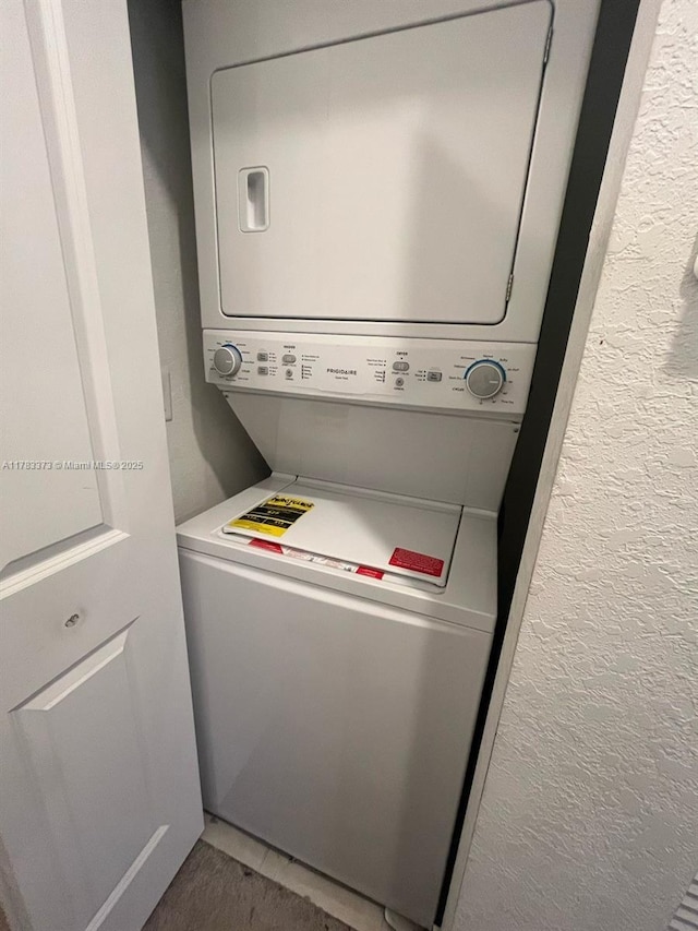 clothes washing area featuring a textured wall, stacked washer / dryer, and laundry area