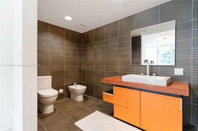 bathroom with a bidet, tile patterned floors, visible vents, toilet, and tile walls