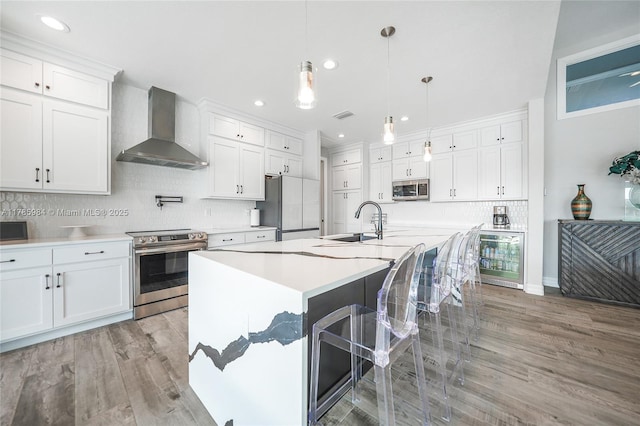 kitchen with beverage cooler, a sink, wall chimney exhaust hood, decorative backsplash, and appliances with stainless steel finishes