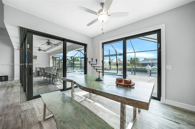 dining space with a water view, light wood finished floors, baseboards, and a ceiling fan