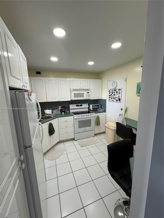 kitchen with white cabinets, dark countertops, light tile patterned flooring, and white appliances