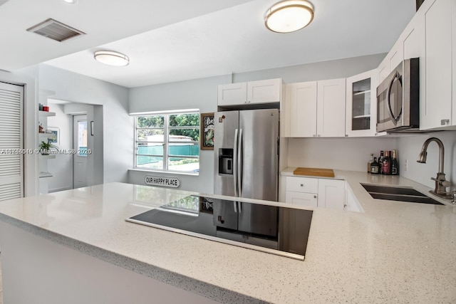 kitchen with appliances with stainless steel finishes, a sink, glass insert cabinets, light stone counters, and white cabinets