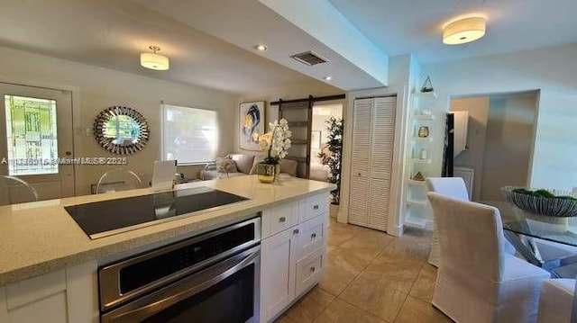 kitchen featuring oven, black electric cooktop, white cabinetry, light countertops, and light tile patterned floors