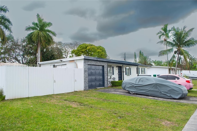 exterior space featuring a front lawn, aphalt driveway, stone siding, an attached garage, and fence