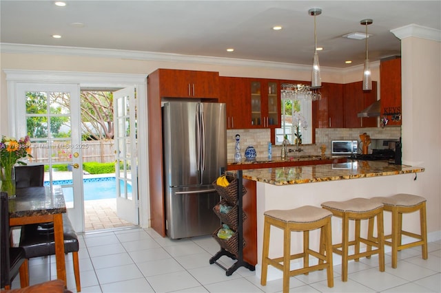 kitchen featuring dark stone countertops, decorative backsplash, a peninsula, glass insert cabinets, and appliances with stainless steel finishes