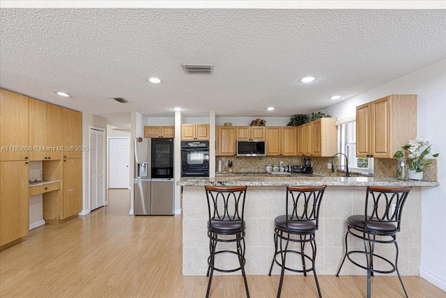 13063 NW 11th Ct, Sunrise, FL 33323 - kitchen with stainless steel appliances, light wood finished floors, a peninsula, a kitchen bar, and a textured ceiling