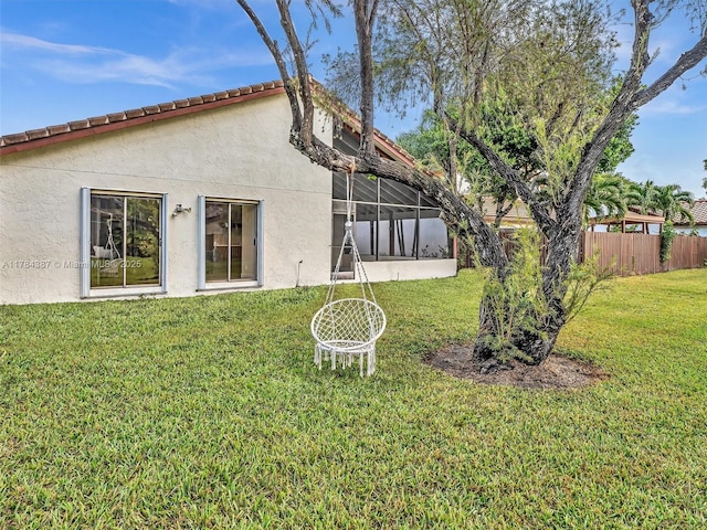 back of property featuring glass enclosure, stucco siding, a yard, and fence
