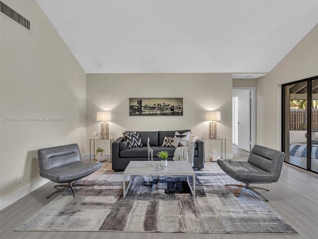 living room featuring baseboards, vaulted ceiling, wood finished floors, and visible vents