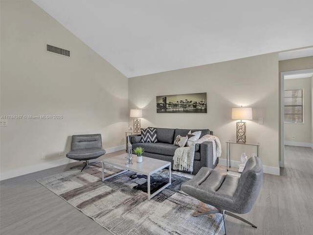 living room with visible vents, baseboards, wood finished floors, and high vaulted ceiling