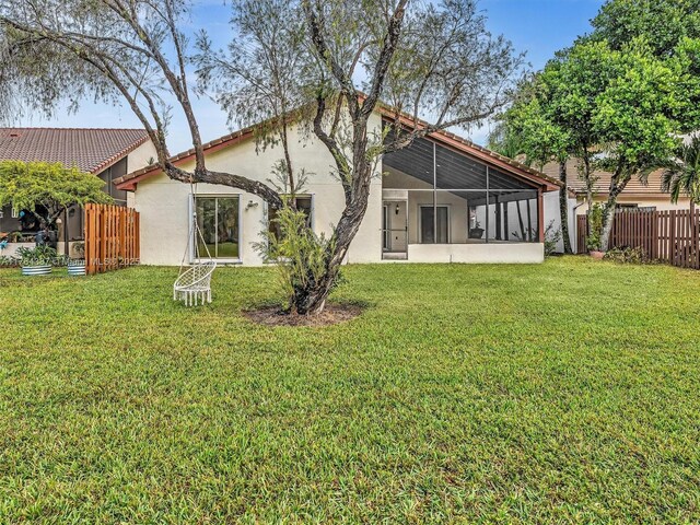 rear view of house with a yard, fence, a sunroom, and stucco siding