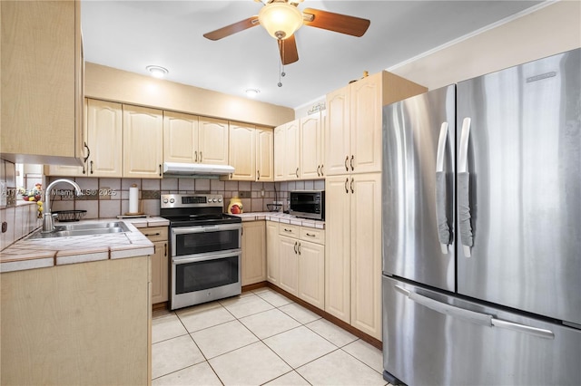 kitchen with under cabinet range hood, tile countertops, light tile patterned floors, a sink, and appliances with stainless steel finishes