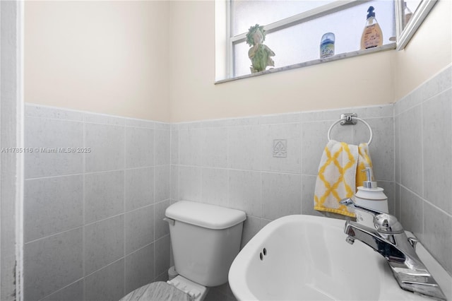 bathroom featuring toilet, a sink, and tile walls