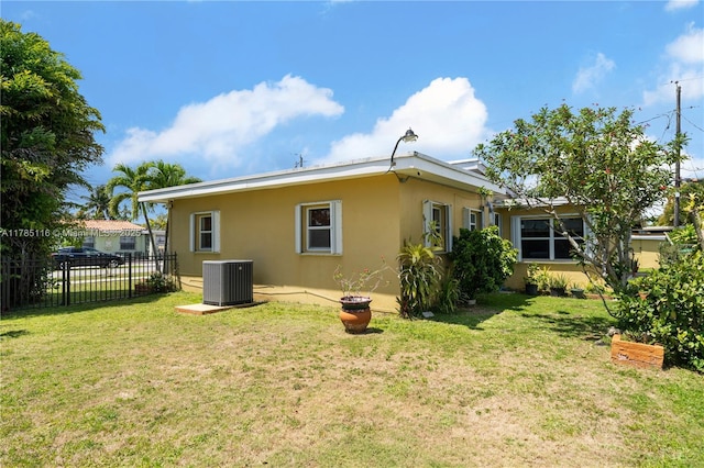 rear view of property with fence, a lawn, central AC, and stucco siding