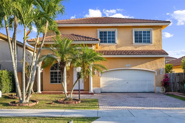mediterranean / spanish-style home with a tiled roof, driveway, fence, an attached garage, and stucco siding