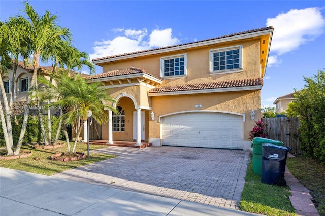 mediterranean / spanish-style house featuring fence, a tiled roof, stucco siding, and decorative driveway