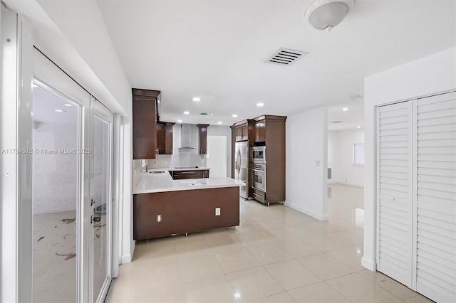 kitchen featuring wall chimney exhaust hood, appliances with stainless steel finishes, dark brown cabinets, and light countertops