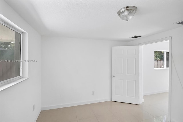 empty room featuring baseboards, tile patterned floors, and visible vents