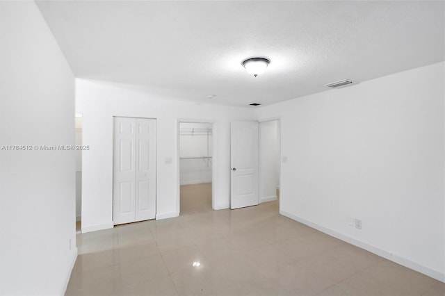 unfurnished bedroom featuring visible vents, baseboards, tile patterned flooring, and a textured ceiling