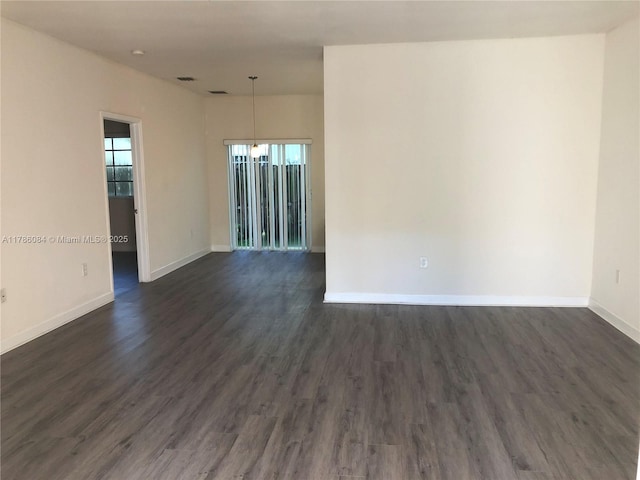 spare room with baseboards and dark wood-style floors