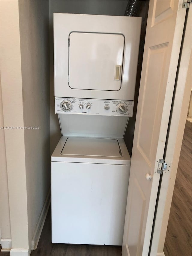 clothes washing area featuring baseboards, stacked washer / drying machine, wood finished floors, and laundry area