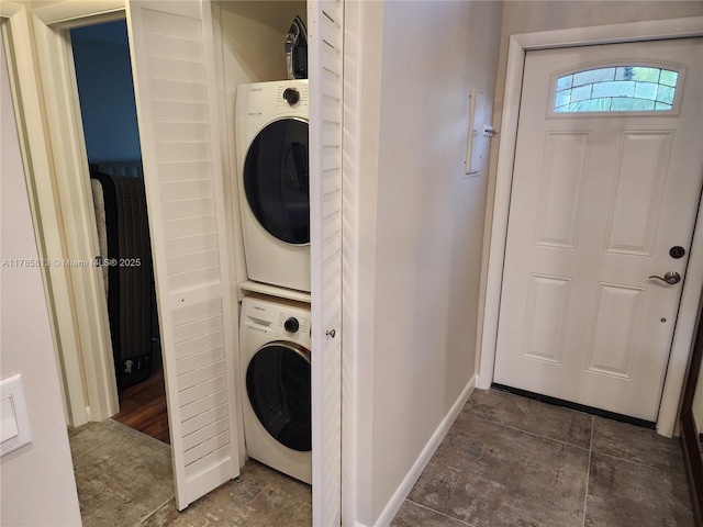 washroom with baseboards, stacked washer and clothes dryer, and laundry area