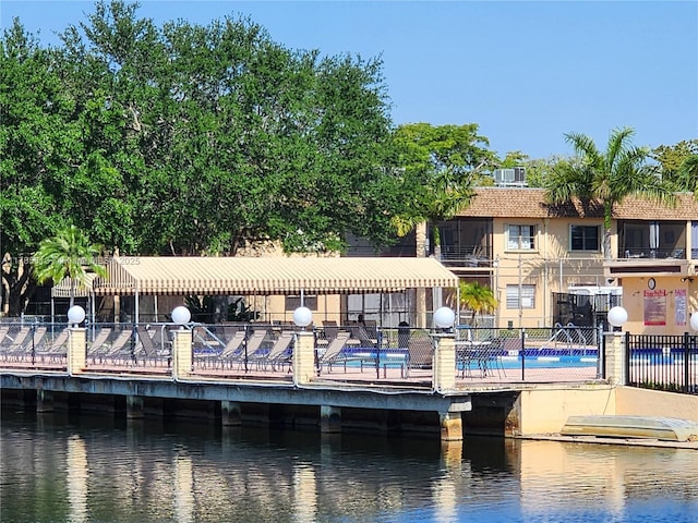 rear view of house with fence, a community pool, and a water view