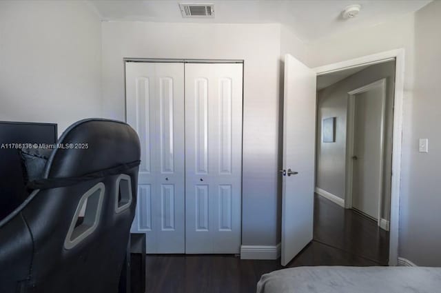 bedroom with baseboards, wood finished floors, visible vents, and a closet