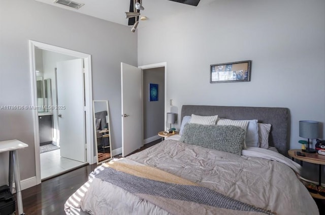 bedroom featuring visible vents, baseboards, ensuite bath, and wood finished floors