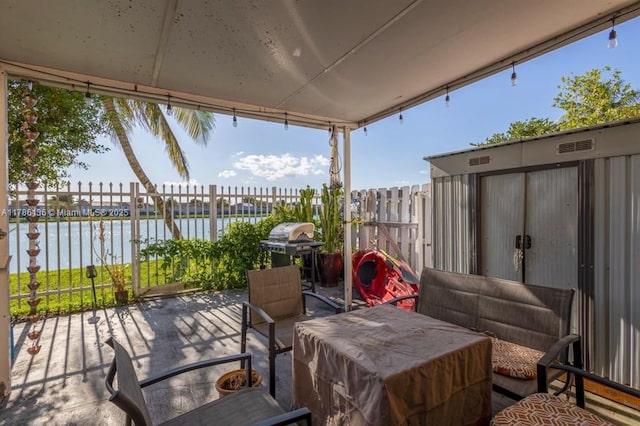 view of patio featuring grilling area, fence, and a water view