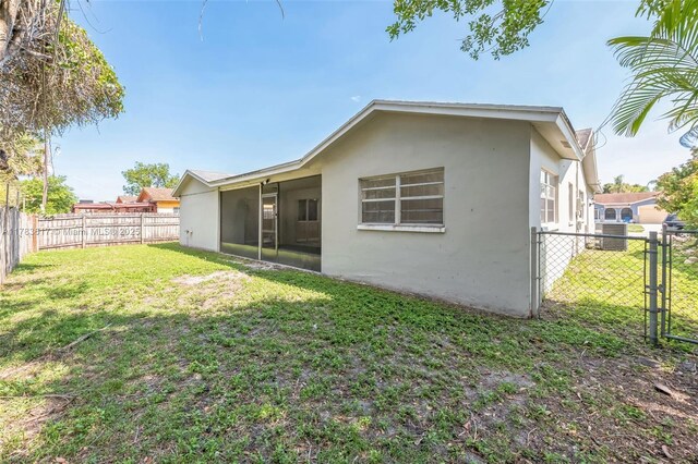9219 SW 1st Pl, Boca Raton, FL 33428 - back of property with a gate, a fenced backyard, stucco siding, a lawn, and a sunroom