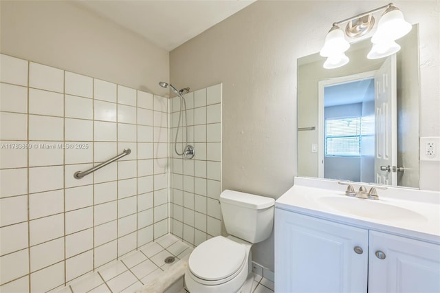 bathroom featuring a tile shower, a textured wall, toilet, and vanity