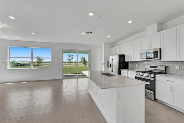 kitchen featuring decorative backsplash, a kitchen island with sink, a sink, stainless steel appliances, and light tile patterned flooring