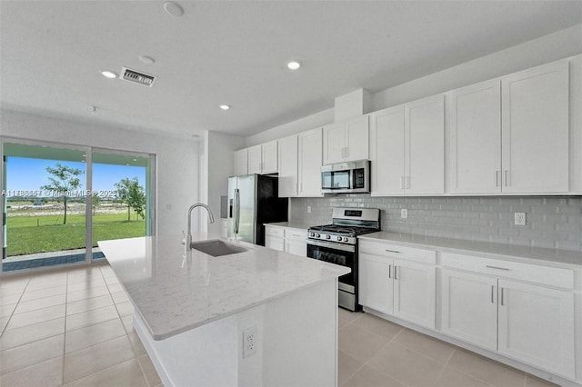 kitchen featuring decorative backsplash, an island with sink, a sink, appliances with stainless steel finishes, and light tile patterned floors