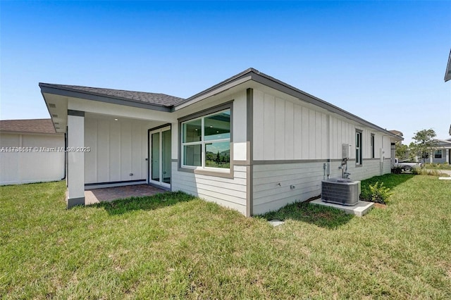 back of property with board and batten siding, a yard, and central AC