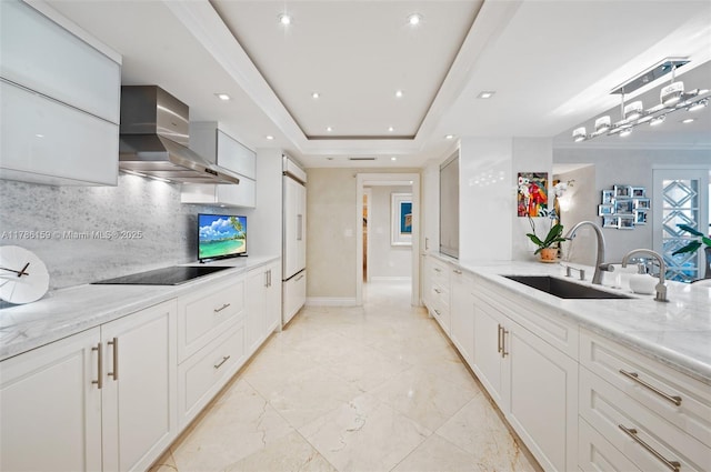 kitchen featuring light stone counters, a sink, wall chimney exhaust hood, black electric stovetop, and tasteful backsplash
