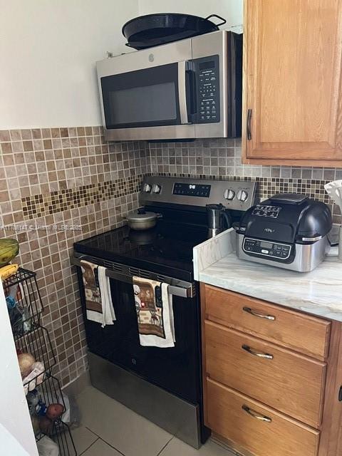 12045 SW 18th St Unit 1-42, Miami, FL 33175 - kitchen with stainless steel microwave, electric range oven, light countertops, brown cabinets, and backsplash